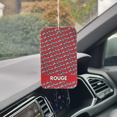 Car air freshener with 'ROUGE' branding hanging from a car's dashboard.