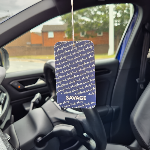 Car air freshener with 'Savage' text hanging from a car's rearview mirror.